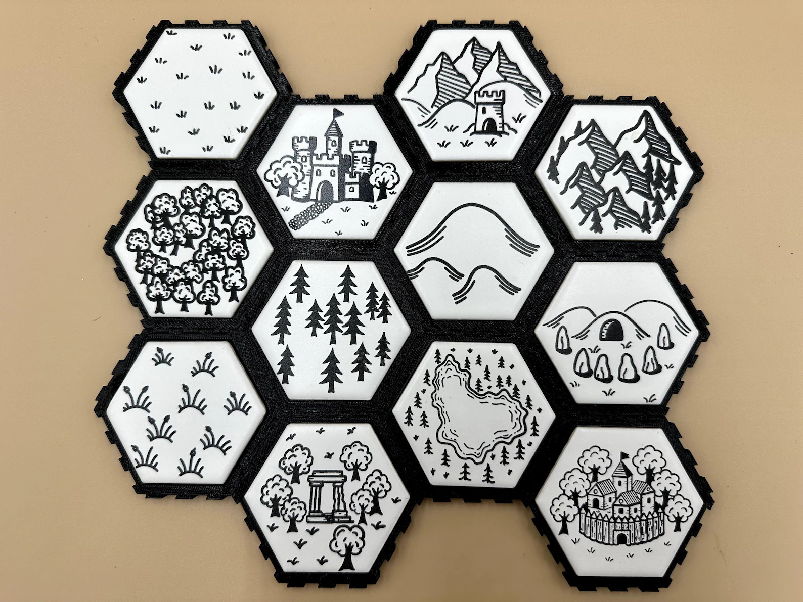 Ceramic laser-etched hex tiles with hand-drawn terrain artwork arranged on a table